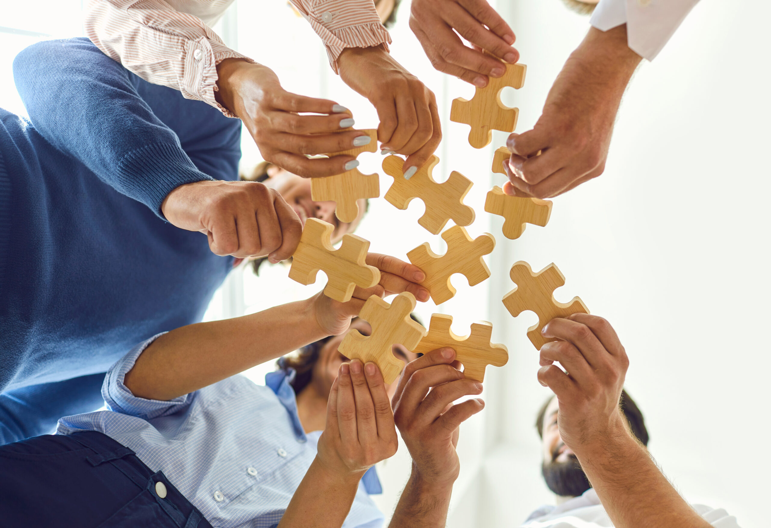 Happy company employees joining parts of jigsaw puzzle during work meeting or team building activity